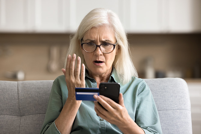 Older woman holding credit card and phone in disbelief